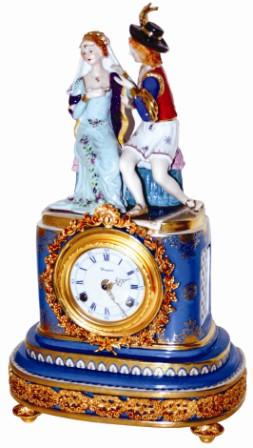 Porcelain figural mantle clock, 18" high, with boy and girl figures. The china case has painted sections, the gold matching the brass sections around the case and around the bezel. — Antique Clocks Price Guide