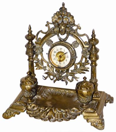 French brass clock/inkwell, ca 1885. The case is 10" wide, 10" high, cast brass with decorations at the top, and a wreath under the clock. — Antique Clocks Price Guide