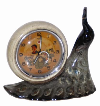 Animated novelty clock that features a ceramic peacock with an alarm clock on its back. The case is 8" wide and almost 8" high. — Antique Clocks Price Guide