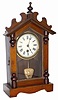 German mantle clock. 16" high walnut case has several wood ornaments and turnings, also ripple around the door.