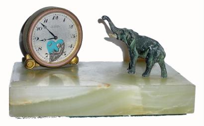 C.1920, Swiss, ÓLe petit ForgeronÒ, desk novelty. In a heart shaped opening in the bottom of the dial sits a little winged cherub making iron arrows at the anvil. His hammer is attached to the lever beneath the dial and appears to hit the anvil with every tick. A little spelter elephant is mounted to the marble base and appears to be looking at the time. — Antique Clocks Price Guide