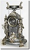 C.1890, French, Silvered Spelter Figural clock, an unusual design with young boys and masks, one boy holding a harp, and the other a writing instrument; the case surmounted by a large urn with two young boys seated on the side handles.