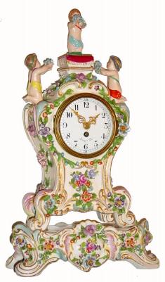 C.1920, French, Leroy and Cie, Porcelain cased timepiece, 3 cherubs over the dial, flowers in relief, and with separate decorated base. — Antique Clocks Price Guide