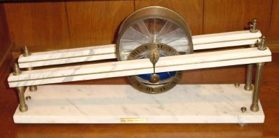 C.1974 (dated) George Dorne's Clepsydra, No. 9, marble base with bronze uprights and brass cylinder with plexi-glass partitions, the blue liquid and the force of gravity on the incline providing the motive force. — Antique Clocks Price Guide