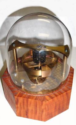 C.1996 (dated), D. J. Moore, Spring detent Escapement model, on a tiger maple base, with American open spring movement as power source held within the base, and with dome. — Antique Clocks Price Guide