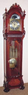 C.1995, American Hall Clock "THE MAJESTIC", 3-weight, cable drive, 8-day, playing your choice of 3 tunes on 9 rods: Whittington, St. Michaels or Westminster, with large lyre/grid iron pendulum, in a mahogany case with burled and carved accents. — Antique Clocks Price Guide