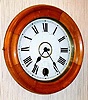 C.1900, New Haven "Eight Day Pendulum Time Clock" in a box case with turned wood bezel, the painted metal dial with a hole at 6 for attending the pendulum.