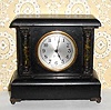 C.1915, Sessions, Bristol, Conn, Mini black mantel clock with faux marble columns to the side and cast metal capitals and feet.
