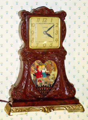 C.1950, United Metal Goods Mfg, Brooklyn, NY, BOY and GIRL ON SWING, 110v electric automaton timepiece in a plastic molded case, with heart shaped opening below the dial. — Antique Clocks Price Guide
