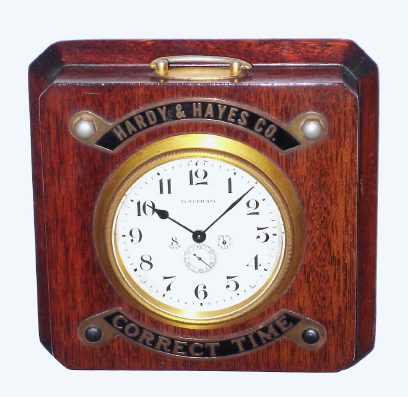 C.1930, Waltham Watch Co., "Waltham Chronometer" model, 8-day back wind with up/down indicator on the dial, mounted in a mahogany case with the "Correct Time" in brass fastened on top. Counter top advertising piece for Hardy and Hayes. — Antique Clocks Price Guide