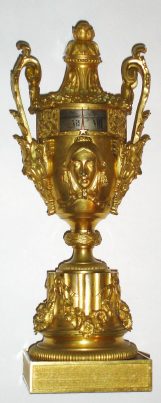 C.1870, French, Gilt Bronze Annular dial clock, in the form of an urn, profusely decorated with female busts, swags and acanthus sprays, the urn atop a fluted round support, the whole setting on a matted square base. — Antique Clocks Price Guide