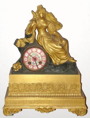 C.1860 French Ormolu Figural Clock: Clock has a colored porcelain dial with a figure of a maiden seated with a dove giving her a peck on the cheek, and an 8-day time and bell strike movement. — Antique Clocks Price Guide