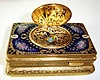 Late 20th Century, German, Singing Bird box, key wound, in an engraved and gilded case with enamel top showing floral decorations and the bird cover with a garden scene with lovers.