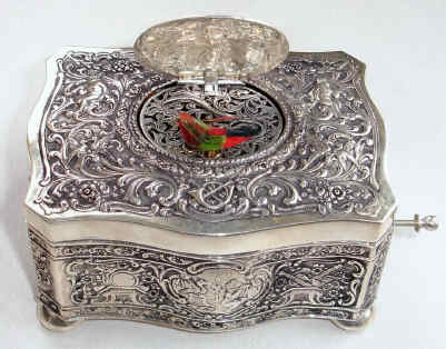 Late 20th Century, German/Swiss, singing bird in a .925 marked coin silver case, embossed with cherubs and birds, and the lid decorated with two putti, one with lyre, the second with music book. — Antique Clocks Price Guide