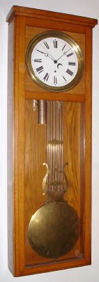 A Swiss or French pinwheel movement with porcelain dial and center seconds, now in an American oak case, probably from a self winding school unit, with grid/lyre pendulum, 8-day. C.1900. — Antique Clocks Price Guide