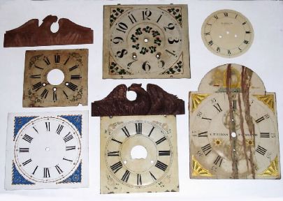 Box lot of 15 wooden dials in various conditions. Two modern eagle splats for wooden movement shelf clocks. A modern striking banjo dial, 1 modern replacement glass for an OG or column clock. Period metal dial. ST tall clock dial, distressed but restorable. — Antique Clocks Price Guide