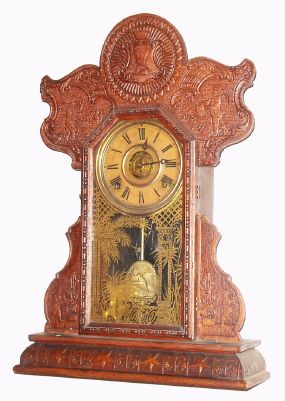 E. Ingraham and Co., "242", 8-day time/strike/alarm oak mantel clock, commemorative series with winged cherubs at work, top left with hammer, anvil and vice, bottom sections w/ cherubs turning a handle on some fanciful contraption, and with an Army/Navy base molding with stars and anchors. Pressed oak case retains its original crazed finish. This was a special order case produced for a customer as indicated on the partial label on the whose name we cannot read. Original paper dial has age darkened. Hands, pendulum and tablet are original. Circa 1905. — Antique Clocks Price Guide