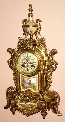 French, S. Marti and Cie, for J. E. Caldwell, Philadelphia, an architectural fantasy with swags, female caryatids and flower adornments, all in cast brass, now polished, and with a porcelain panel dial showing a winged cherub, a plaque below the dial showing a pair of lovers and a ladies' bust on the porcelain urn at top, 8-day time and strike, spring movement. C.1900 — Antique Clocks Price Guide