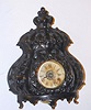 American cast and pierced iron cased alarm clock, under a round glass dome w/ base from the same period. C.1900.