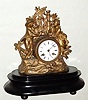 French, S. Marti et Cie, cast spelter figural mantel clock, with patinated gold appearing finish, showing a boy offering a nest of eggs to a girl with a basket of roses, 8-day, bell strike, mounted to a wooden base (no dome) C.1900