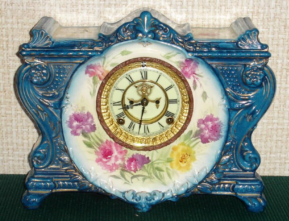 Ansonia Clock Co., C.1900, Royal Bonn, "LA VINDA" porcelain china cased clock, with 8-day, gong strike mov't with open escapement on porcelain dial. Case is dark aqua with fields of cream decorated with magenta and yellow flowers. — Antique Clocks Price Guide