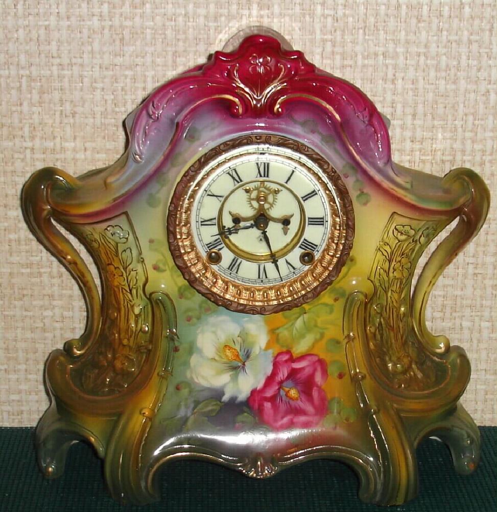 Ansonia Clock Co., C.1910, Royal Bonn, "LA LAYON" porcelain china cased clock, with 8-day, gong strike mov't with open escapement on porcelain dial, in a multi-colored case, red top, yellow center + dark green at base, with two large peonies below the dial, red and white. — Antique Clocks Price Guide