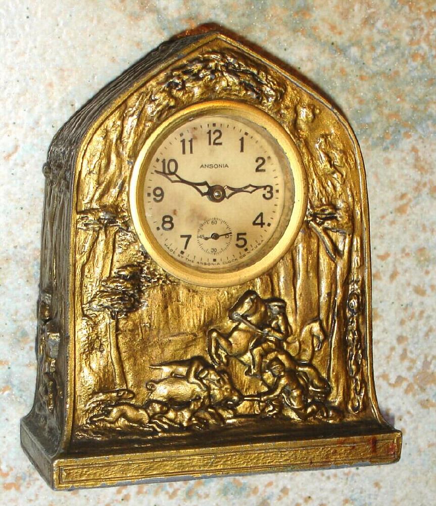 Ansonia Clock Co., cast pot metal BANK novelty, the case depicting dogs and horseback hunters capturing a wild boar, and the back with slots for coins and a key lock door to remove the money [no key], c.1910 — Antique Clocks Price Guide
