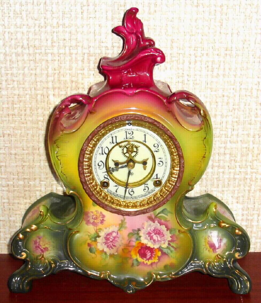 Ansonia Clock Co., C.1905, Royal Bonn, "LA VENDEE" porcelain china cased clock, with 8-day, gong strike mov't with open escapement on porcelain dial, in a tri-colored case, red top, lime-yellow center + dark green at base, with multi colored floral decorations on the lower front and sides. — Antique Clocks Price Guide