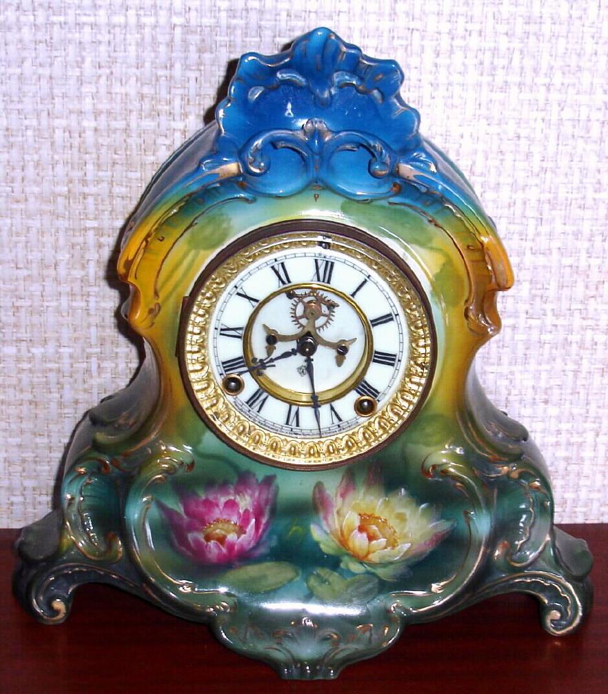 Ansonia Clock Co., C.1905, Royal Bonn, "LA NORMANDIE" porcelain china cased clock, with 8-day, gong strike mov't with open escapement on porcelain dial, in a TRI-colored case, aqua/green top, yellow center + dark green at base, with pink and yellow water lily blossoms below the dial. — Antique Clocks Price Guide
