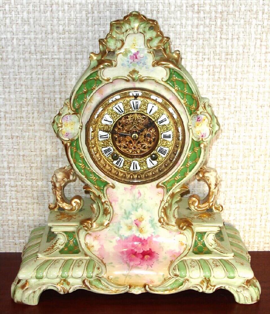 Ansonia Clock Co., C.1905, Royal Bonn, "LA CERDA" porcelain china cased clock, with 8-day, gong strike mov't with open escapement on porcelain dial, in a tri-colored case, cream base, with light green edges and darker green accents, with multi-colored floral decorations. Bonn logo on case back in gold. — Antique Clocks Price Guide