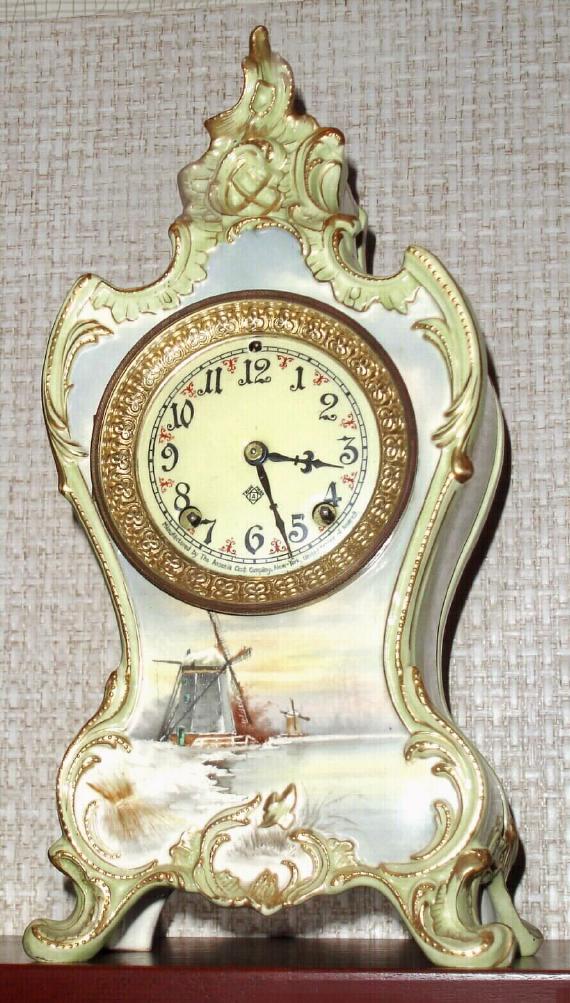 Ansonia Clock Co., C.1895, Royal Bonn, "LA BOURGOGNE" porcelain china cased clock, with 8-day, gong strike mov't with one piece creamy dial with red trim between the numerals, and the lower scene of a Dutch harbor with sailing ship. — Antique Clocks Price Guide