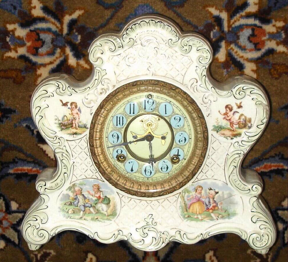 Ansonia Clock Co., unknown porcelain model, probably a Wringer premium, with 4 small cameos of children at play {fishing in lower rt cameo}. Best part of this clock is the rare porcelain dial with Arabic numerals on blue circular fields — Antique Clocks Price Guide
