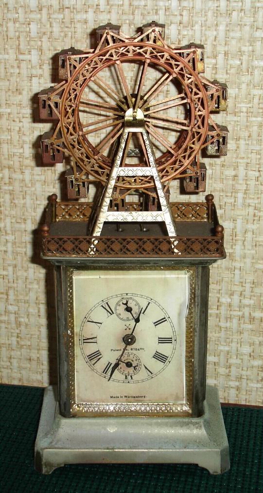 German, Hamburg American [crossed arrow trademark], C.1910, novelty with large Ferris wheel that goes 'round while the clock is running. This is a one day time and alarm, also with seconds hand. — Antique Clocks Price Guide