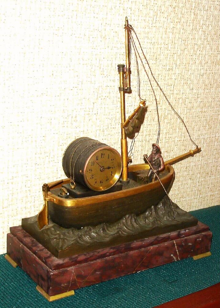 French, OARSMAN automaton timepiece, C.1885, a bronze sailboat setting on a nest of waves [also bronze], with the lone boatman rowing the boat due to lack of wind. The oarsman is suspended on a tri-leaf "swinger" type suspension, and the assembly is a compound pendulum, with a threaded bob at the bottom for adjustment. — Antique Clocks Price Guide