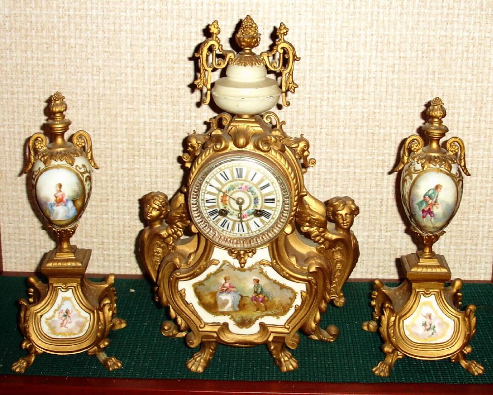 French, S. Marti, 3-piece garniture, gold painted white metal, with hand painted plaques and side urns, 8-day, strike, with fancy painted dial with floral wreath and gilt brass hands. — Antique Clocks Price Guide