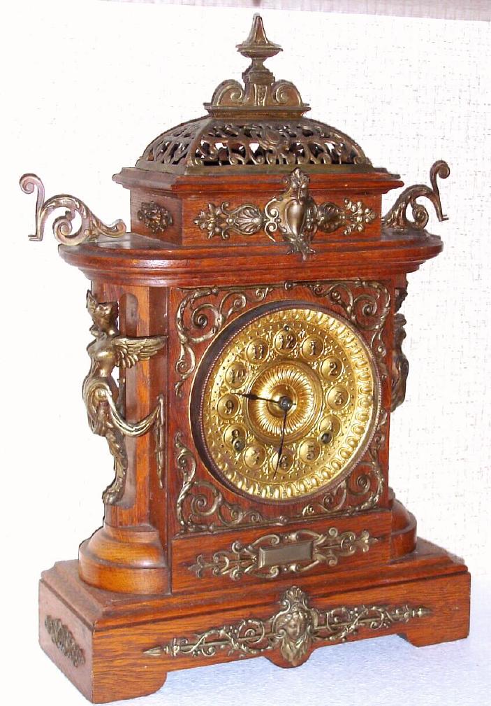 Ansonia Clock Co., New York, C.1894, "CABINET - E", antique oak cased mantle clock with brass trimmings. Has fancy embossed brass dial with raised Arabic numerals, painted black. — Antique Clocks Price Guide
