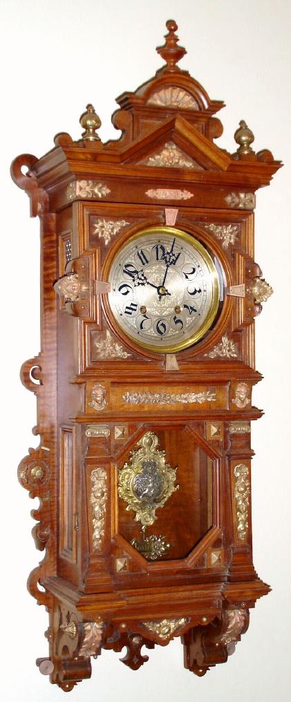 German, Lenzkirch, Walnut cased wall clock with profuse gilt bronze trim, 8-day spring movement, gong striking with extra fancy cast and chased baroque style pendulum with a silvered cherub in the center. — Antique Clocks Price Guide