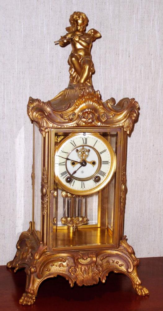 Ansonia Clock Co., New York, C.1910, "EULOGY", 4-Glass crystal regulator, surmounted by a winged cherub playing a flute. With 8-day gong strike movement with open escapement on the porcelain dial. — Antique Clocks Price Guide