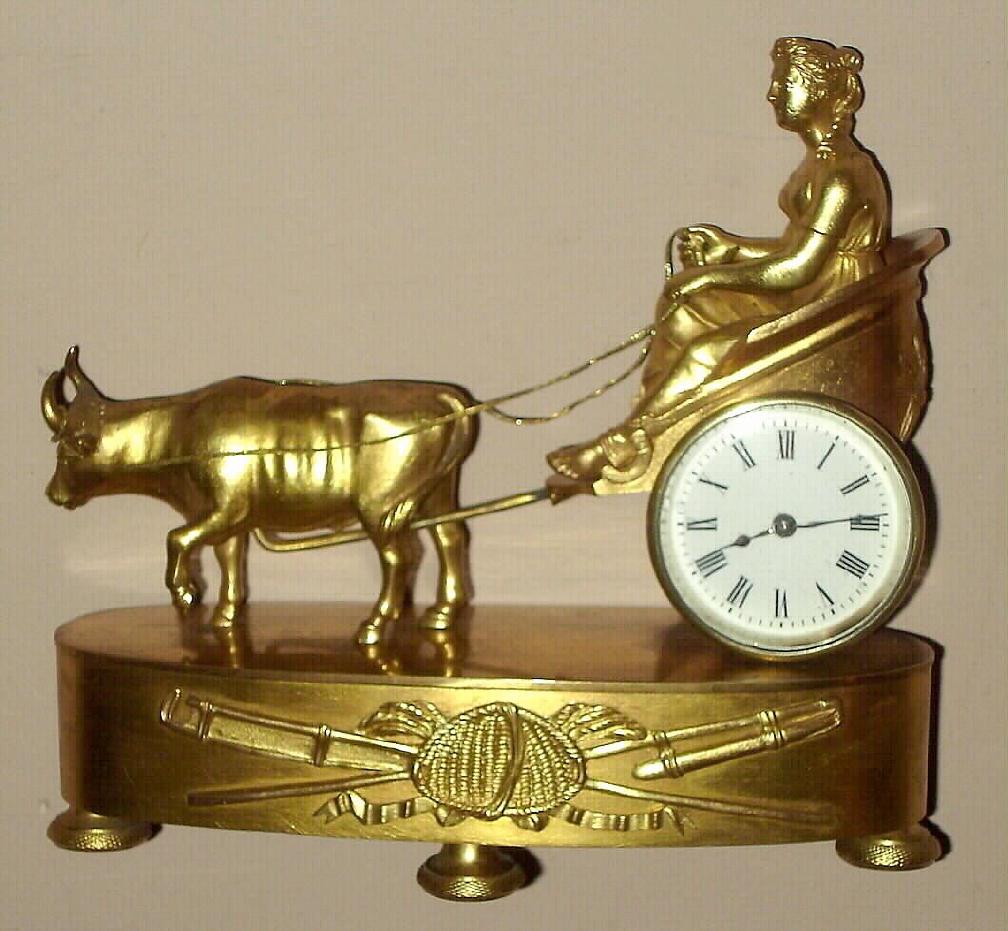 Miniature French gilded brass figural table clock time only spring driven mvt with figure of Greek or Roman lady being drawn by ox cart with Roman numeral porcelain 2" dial, c1850 sNo. 18454 — Antique Clocks Price Guide