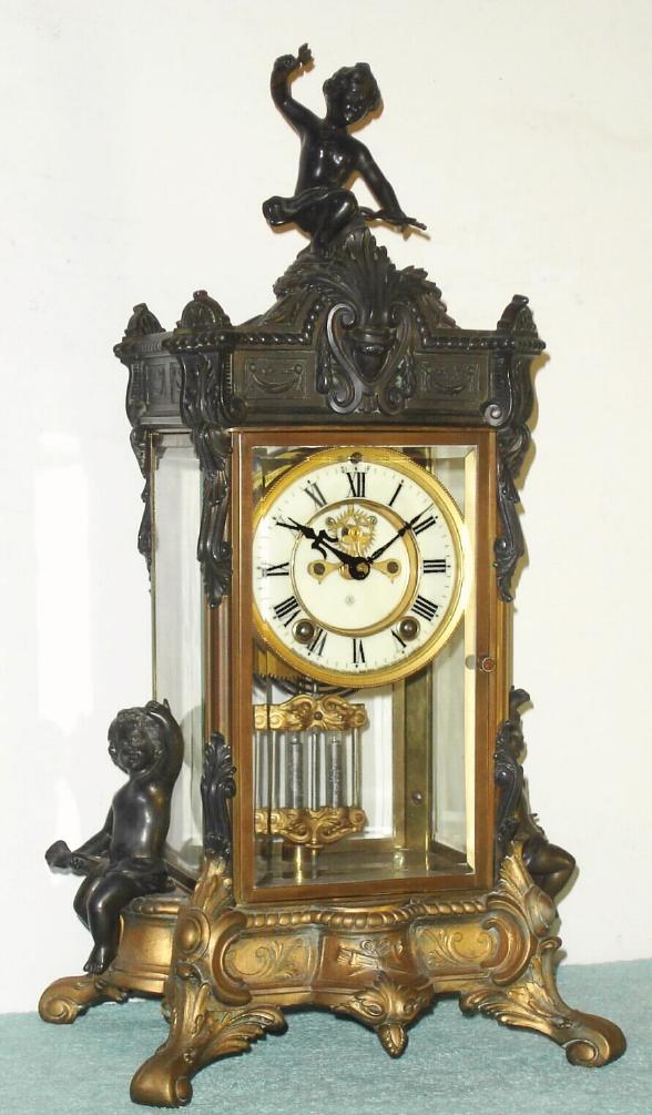 Ansonia Clock Co., 4-Glass crystal regulator, PEERLESS, with 3 figures, Cupid at top [with arrow still attached], and the case flanked by 2 other cherubs, open escapement on the dial and gong striking, C.1905 — Antique Clocks Price Guide