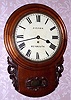 English, single train, chain fusee dial clock, C.1870, in a round top, short drop wall case of mahogany, 8-day with carved accents and a bottom door to access the pendulum, retailed by "Brown" of Weymouth.