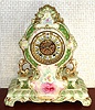 Ansonia Clock Co., C.1905, Royal Bonn, "LA CERDA" porcelain china cased clock, with 8-day, gong strike mov't with open escapement on porcelain dial, in a tri-colored case, cream base, with light green edges and darker green accents, with multi-colored floral decorations. Bonn logo on case back in gold.