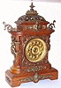 Ansonia Clock Co., New York, C.1894, "CABINET - E", antique oak cased mantle clock with brass trimmings. Has fancy embossed brass dial with raised Arabic numerals, painted black.