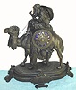 French figural white metal mantel clock, Arabic motif depicting Bedouin at the reins of his blanket clad camel. Dial has applied gilt Roman numerals on blue enamel plaques and base has plaque with Arabic inscription, time and strike on bell 8 day spring driven mvt. {with pendulum} C.1875.