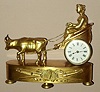 Miniature French gilded brass figural table clock time only spring driven mvt with figure of Greek or Roman lady being drawn by ox cart with Roman numeral porcelain 2" dial, c1850 sNo. 18454