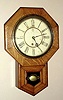 Waterbury Clock Co. Waterbury, Conn. "DROP OCTAGON 10 INCH" wall clock with 8 day time only spring driven mvt in oak veneer case with Roman numeral painted zinc pan 10" dial, C.1910