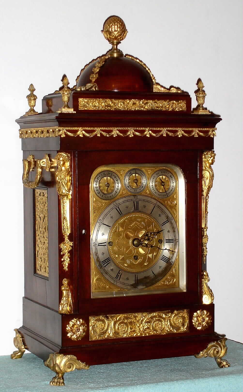 English, mahogany cased Victorian, triple fusee chiming bracket clock, playing your choice of Whittington tune on 8 bells or Westminster on 4 heavy flat-wire gongs, and then counting the hours on a large deep-toned cathedral gong. The impressive case with ormolu caryatids to the corners surmounted by a large pineapple finial, surrounded by 4 flame finials. The finely engraved dial plate is gilded and with subsidiary dials for chime-silent, F/S and tune selection. — Antique Clocks Price Guide