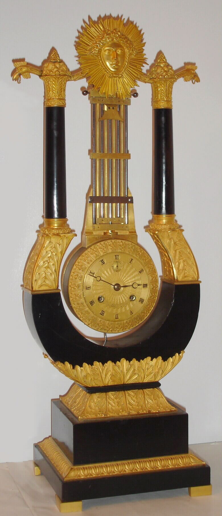 French, lyre form mantel clock, ebonized wood case with ormolu mountings, the pinwheel movement contained within the base of the gird iron pendulum, which has knife edge suspension, the entire movement and pendulum swinging as a single unit. Gilt engine turned dial with painted roman numerals and seconds hand, C. 1840 — Antique Clocks Price Guide