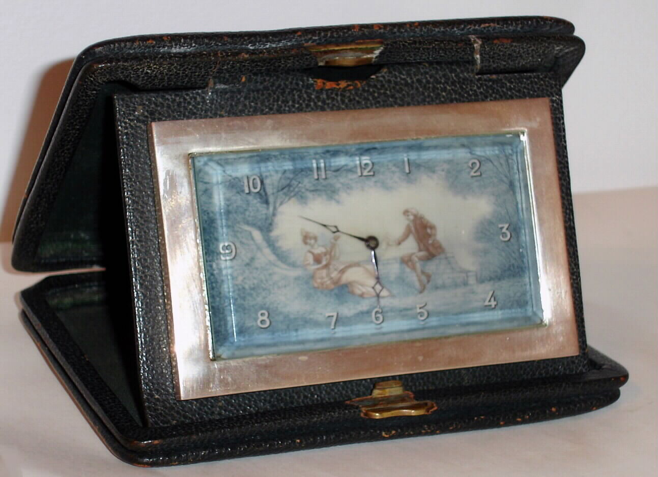 Travel clock Swiss 8 day in silver case with painted ivory Arabic numeral dial decorated in two tone scene of lovers reclining and playing music, c1920 including outer leather travel case — Antique Clocks Price Guide