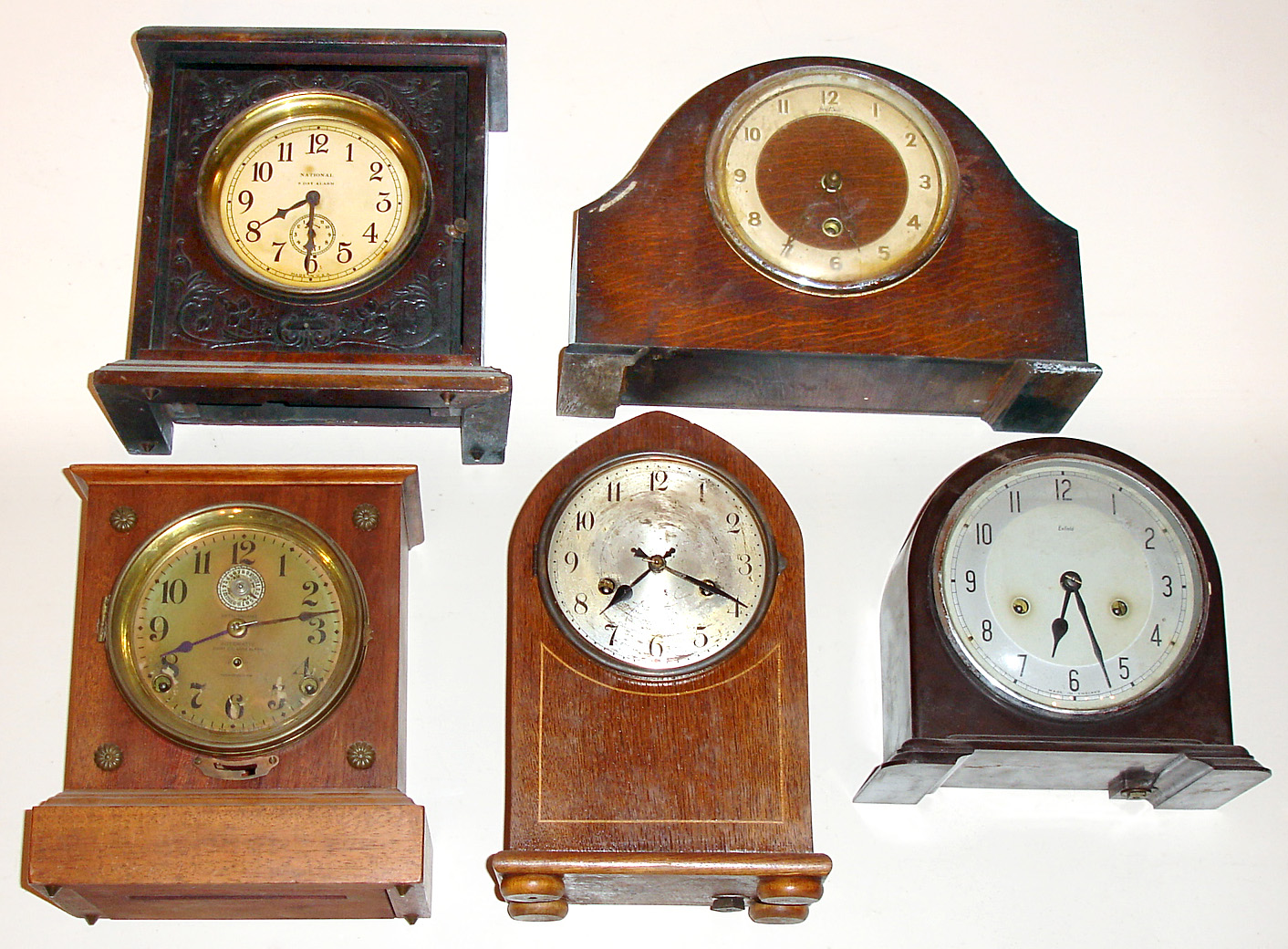 Five wood case 8-day mantel clocks. Two from England (Enfield and Davall), alarm clocks by Seth Thomas and National. Tallest, unsigned, is 11" high — Antique Clocks Price Guide